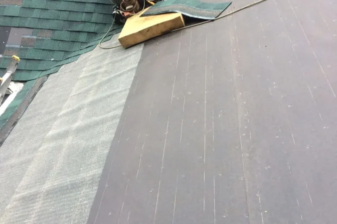 roofing contractor laying new green asphlat shingles on the roof
