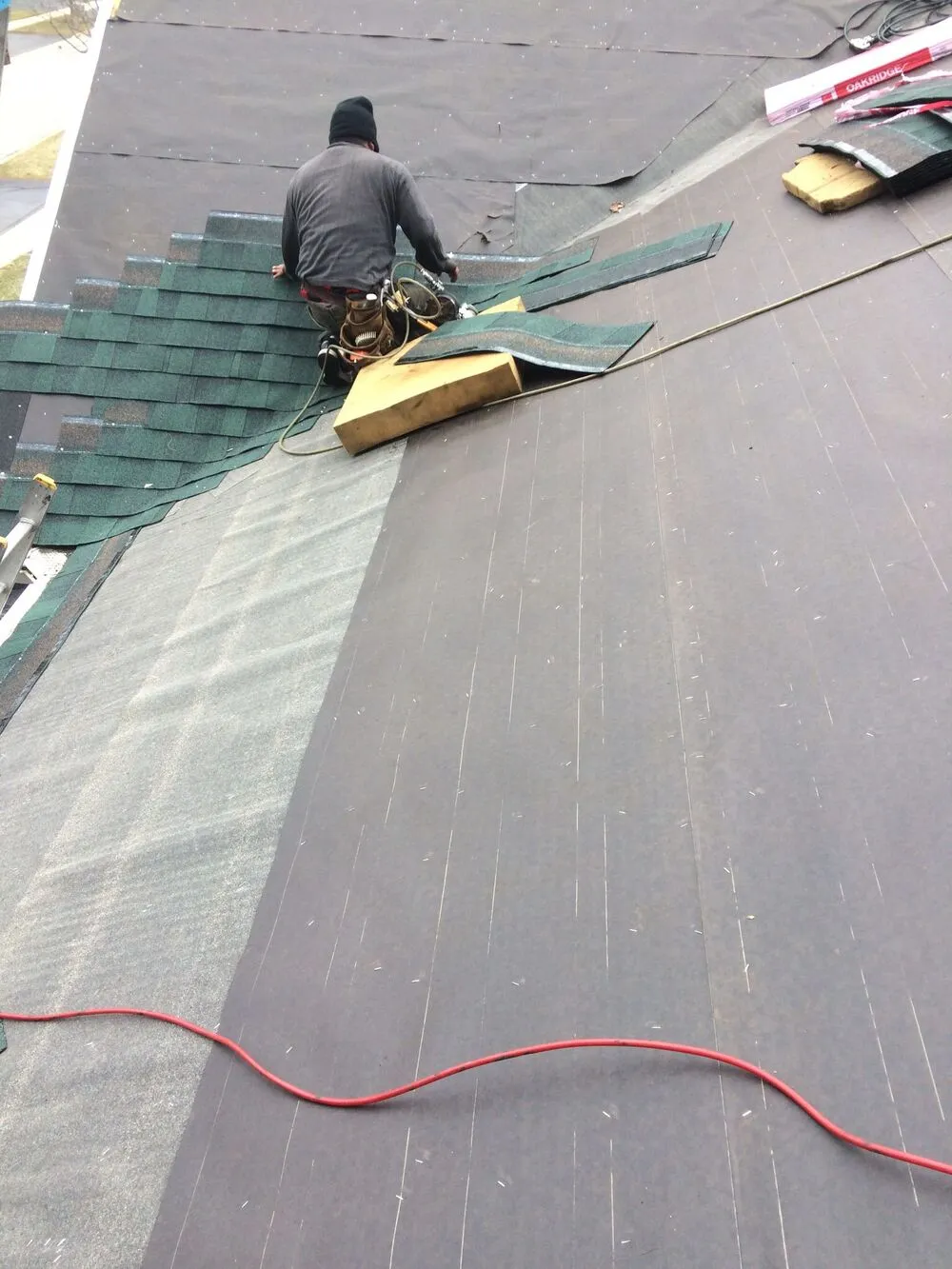 roofing contractor laying new green asphlat shingles on the roof